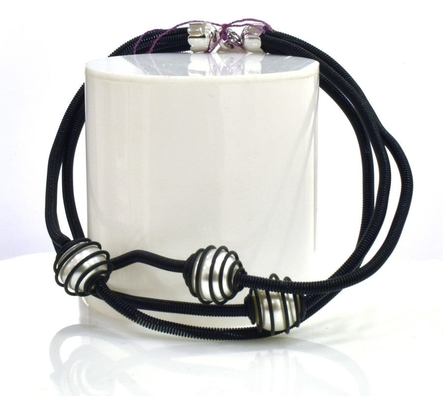 Bracelet PERLE EN CAGE, no 73, de l'artiste Sandrine Giraud. Couleur noir et perles blanches. Ce bijou marie avec élégance la grâce et l’originalité des lignes.