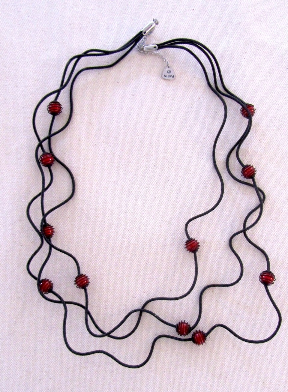 Collier PERLES EN CAGE rouges, no 100, de l'artiste Sandrine Giraud, Ce bijou modulable, toujours original, marie avec élégance la grâce des perles avec l’originalité des lignes résolument contemporaines.